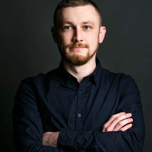 Dark blonde bearded man crosses his hands on chest posing in black shirt